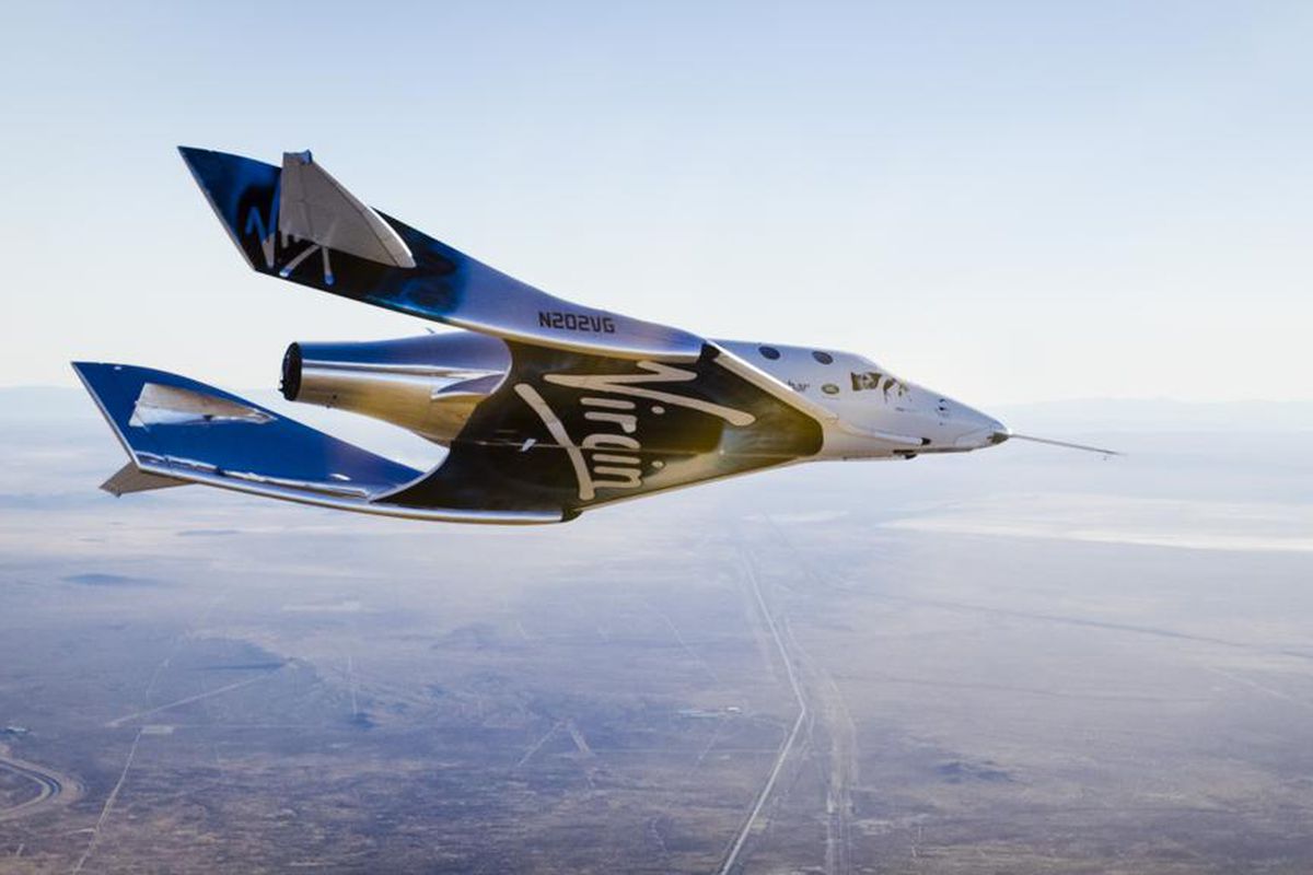 Virgin Galactic's futuristic Space Plane in flight over the Mojave Desert. The underside displays the Virgin Group logo.